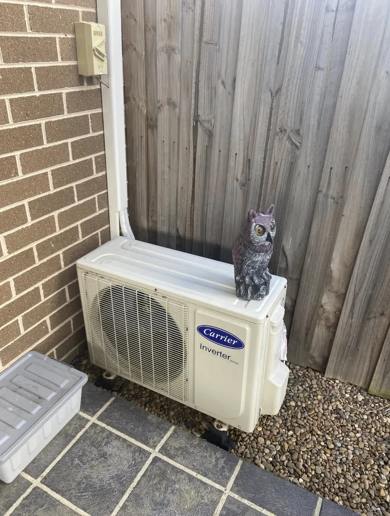 Air conditioning condenser mounted beside a timber fence with clear airflow around it